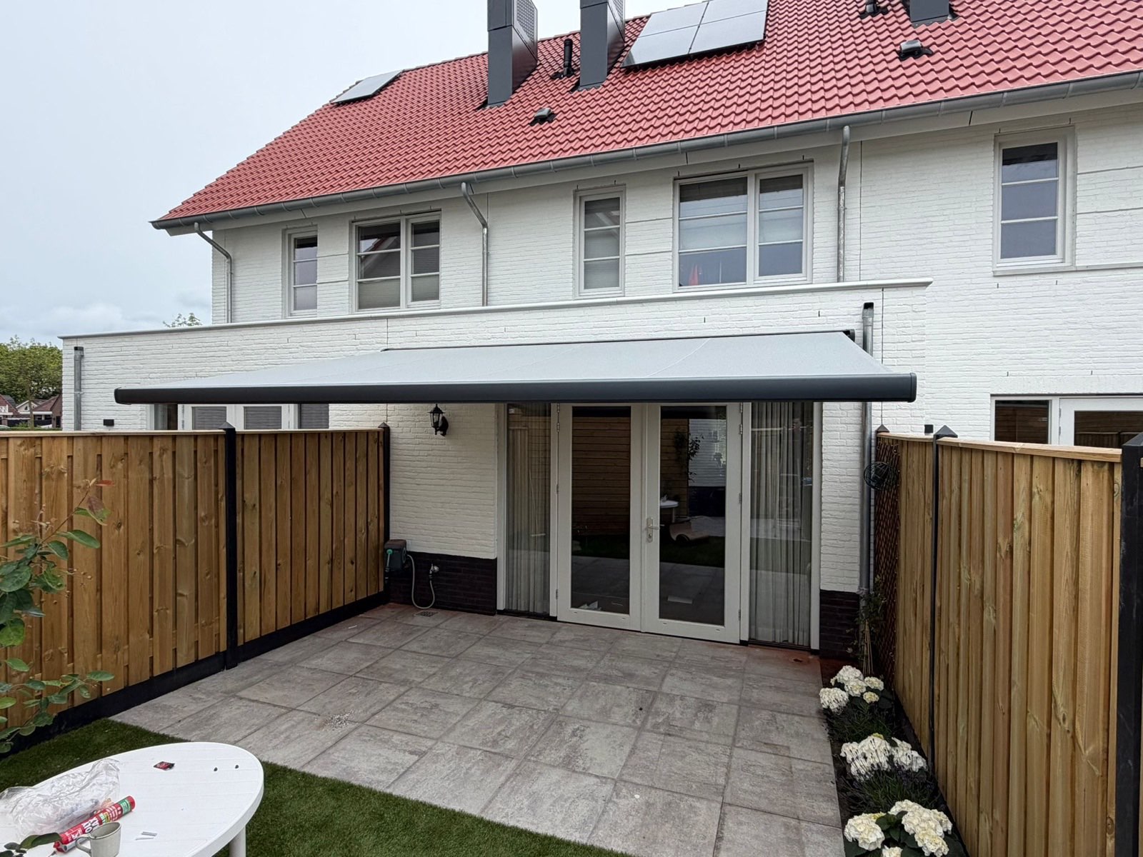 Grijze knikarmscherm boven een terras aan een witte woning